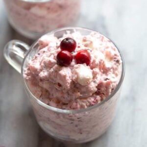 A clear cup full of cranberry salad fluff with three fresh cranberries on top.