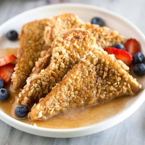 Four slices of crunchy french toast on a plate with berries and syrup.