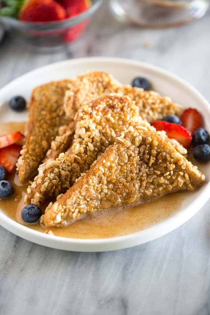 Four slices of crunchy french toast on a plate with berries and syrup.