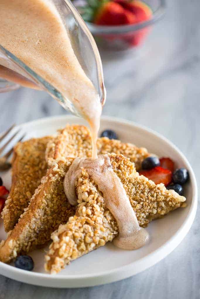 Syrup being poured over french toast on a plate with berries.