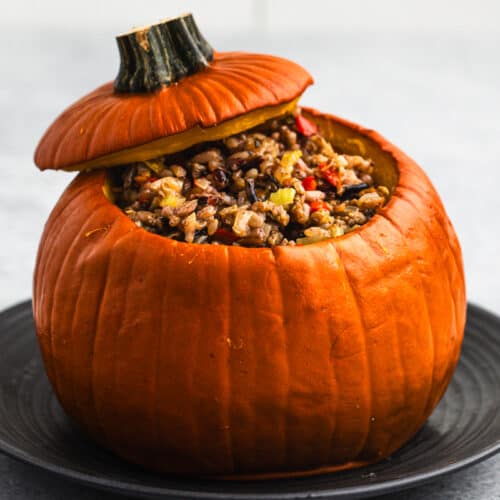 A festive Dinner in a Pumpkin made of wild rice, sausage, and veggies inside a pie pumpkin on a plate.