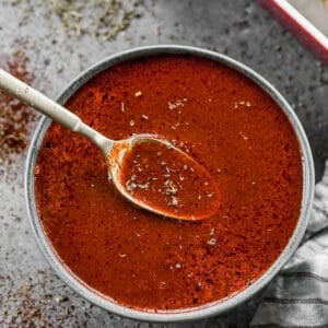 A bowl of homemade enchilada sauce with a spoon in it, lifting some out.