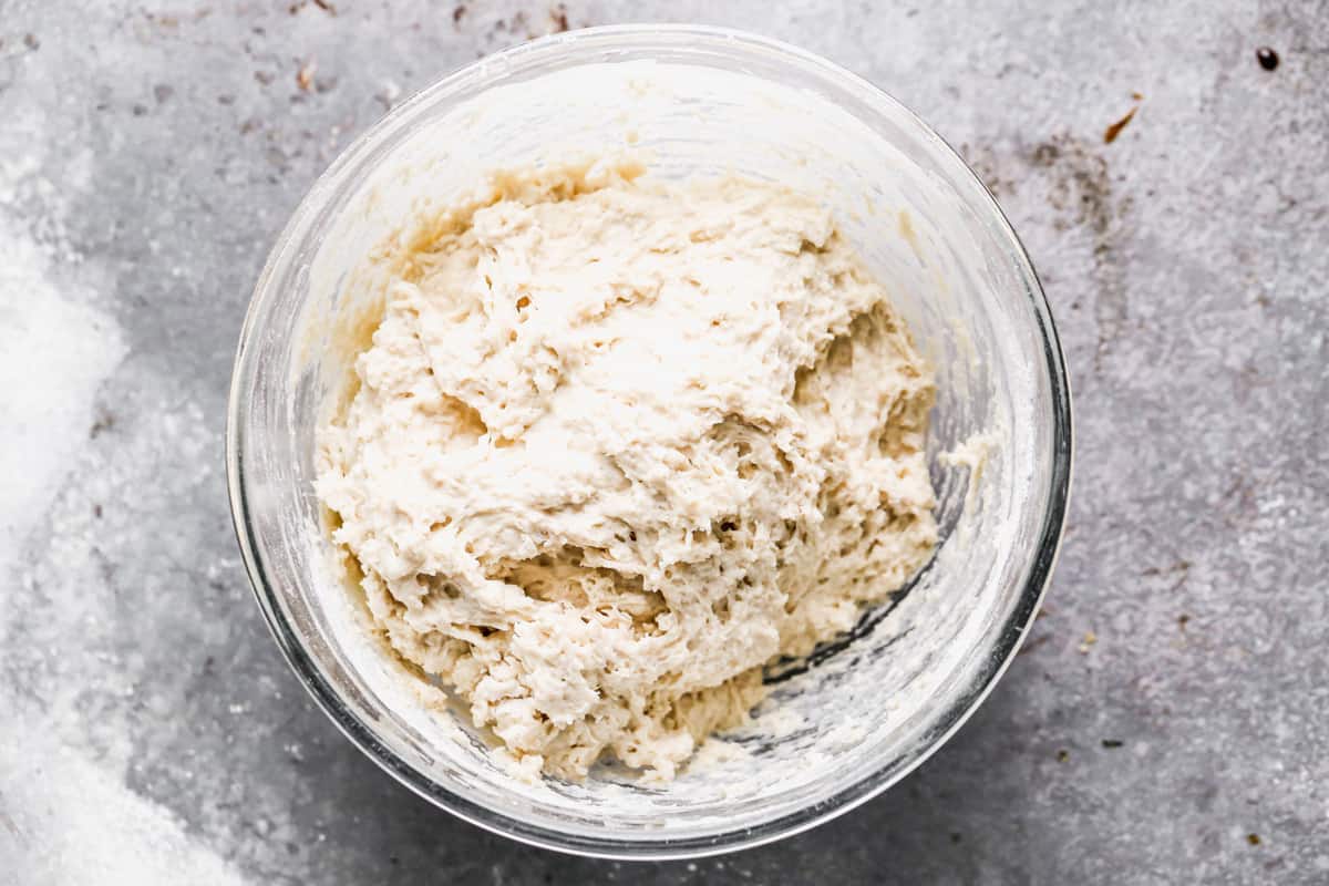 A sticky dough resting in a glass bowl for an easy English Muffin recipe.