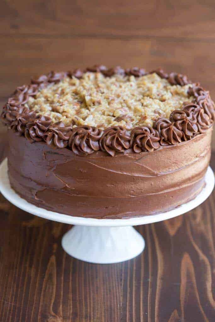 A full frosted and decorated German Chocolate served on a white cake stand.