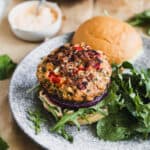 A Greek Turkey Burger on a plate with a homemade feta aioli, charred red onion, and fresh arugula.