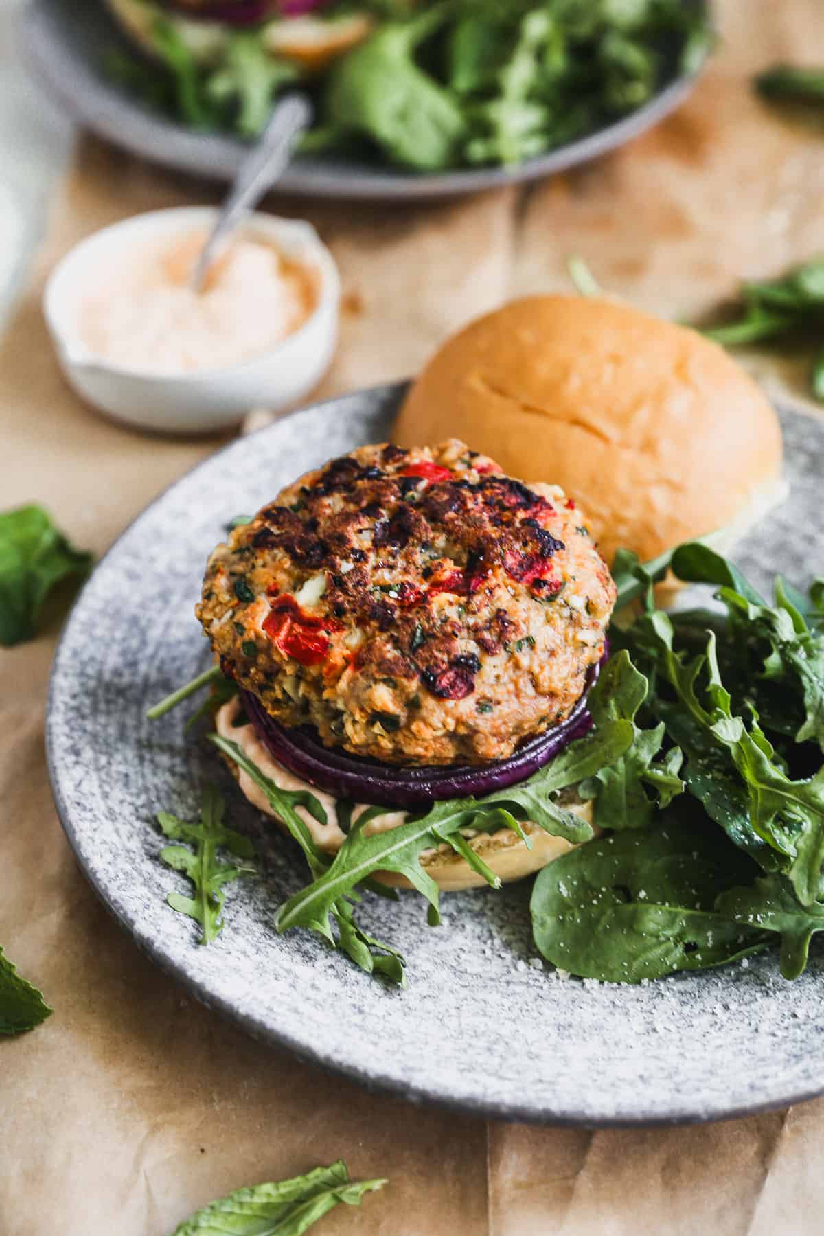 A Greek Turkey Burger on a plate with a homemade feta aioli, charred red onion, and fresh arugula.