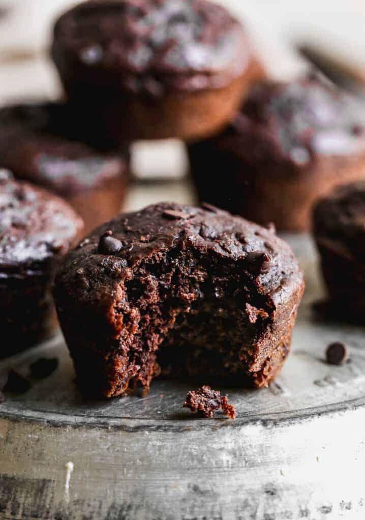 Healthy Chocolate Muffins stacked on a plate with a bite taken out of one, showing the inside muffin crumb..