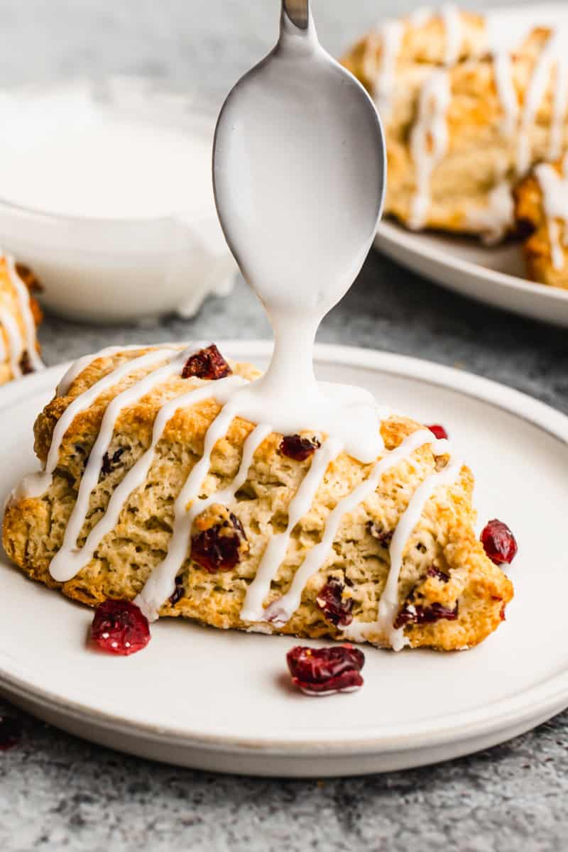 An easy scone recipe with craisins on a plate with glaze being drizzled on top.