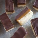 Homemade twix bars with layers of shortbread, caramel and chocolate, cut into rectangles, placed on a grey board.