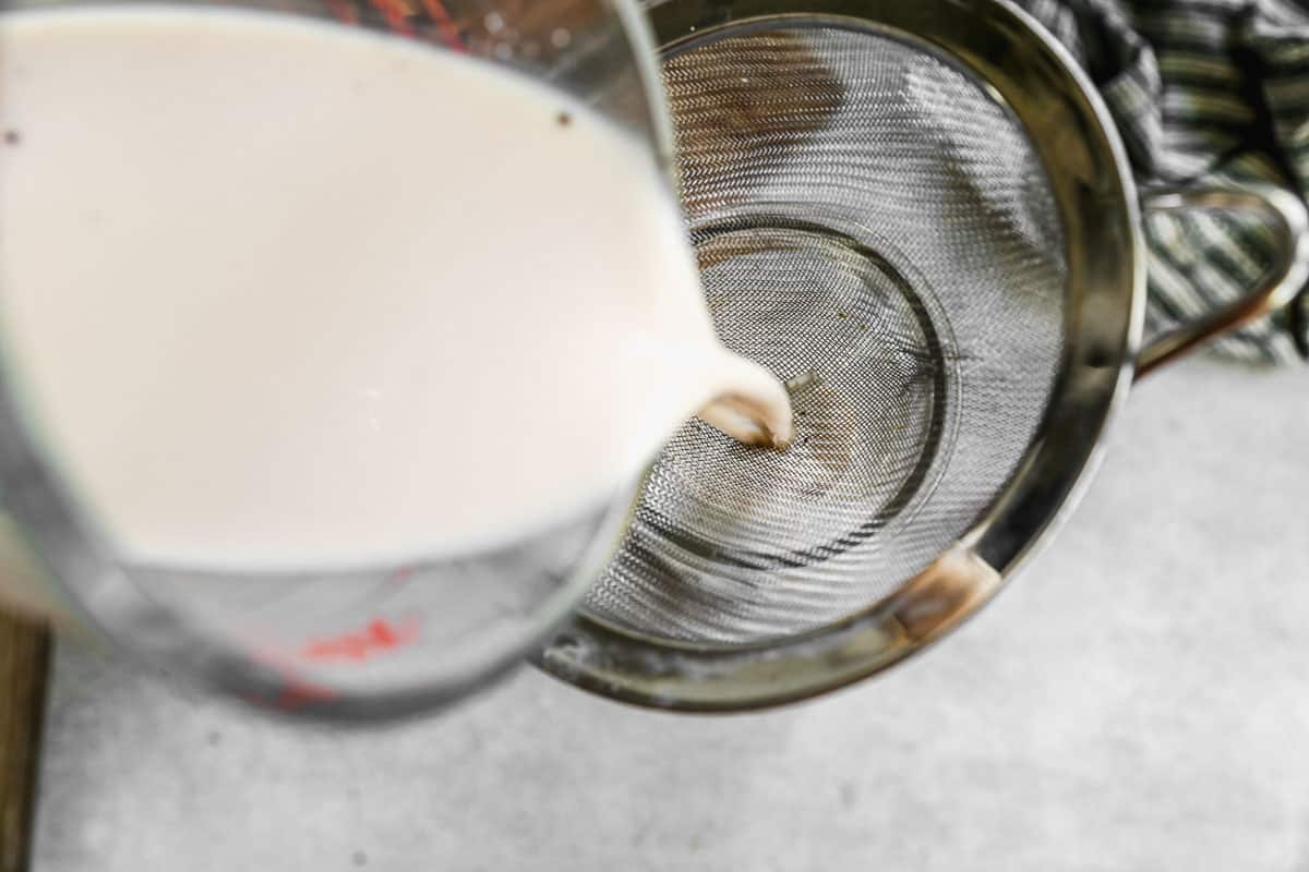 Horchata being poured into a glass through a fine mesh strainer.