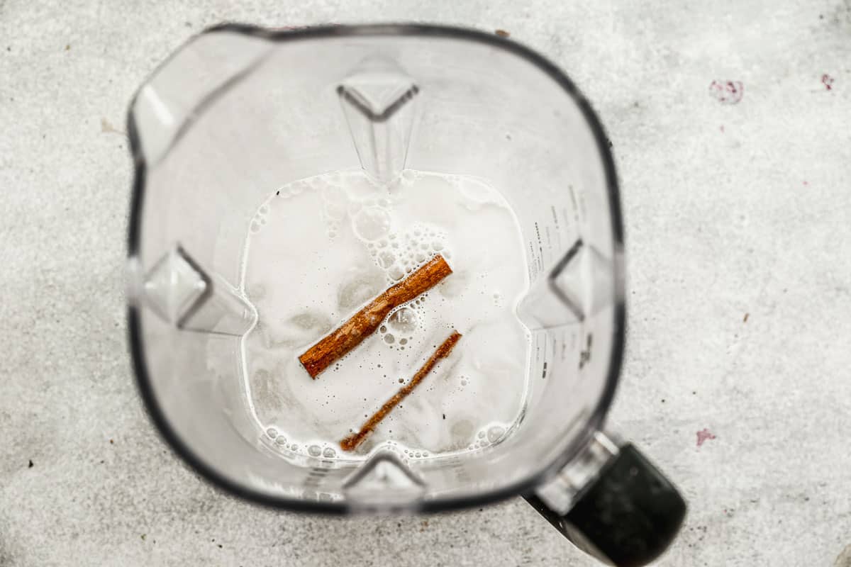 A blender filled with rice, hot water, and cinnamon sticks to make homemade Horchata.