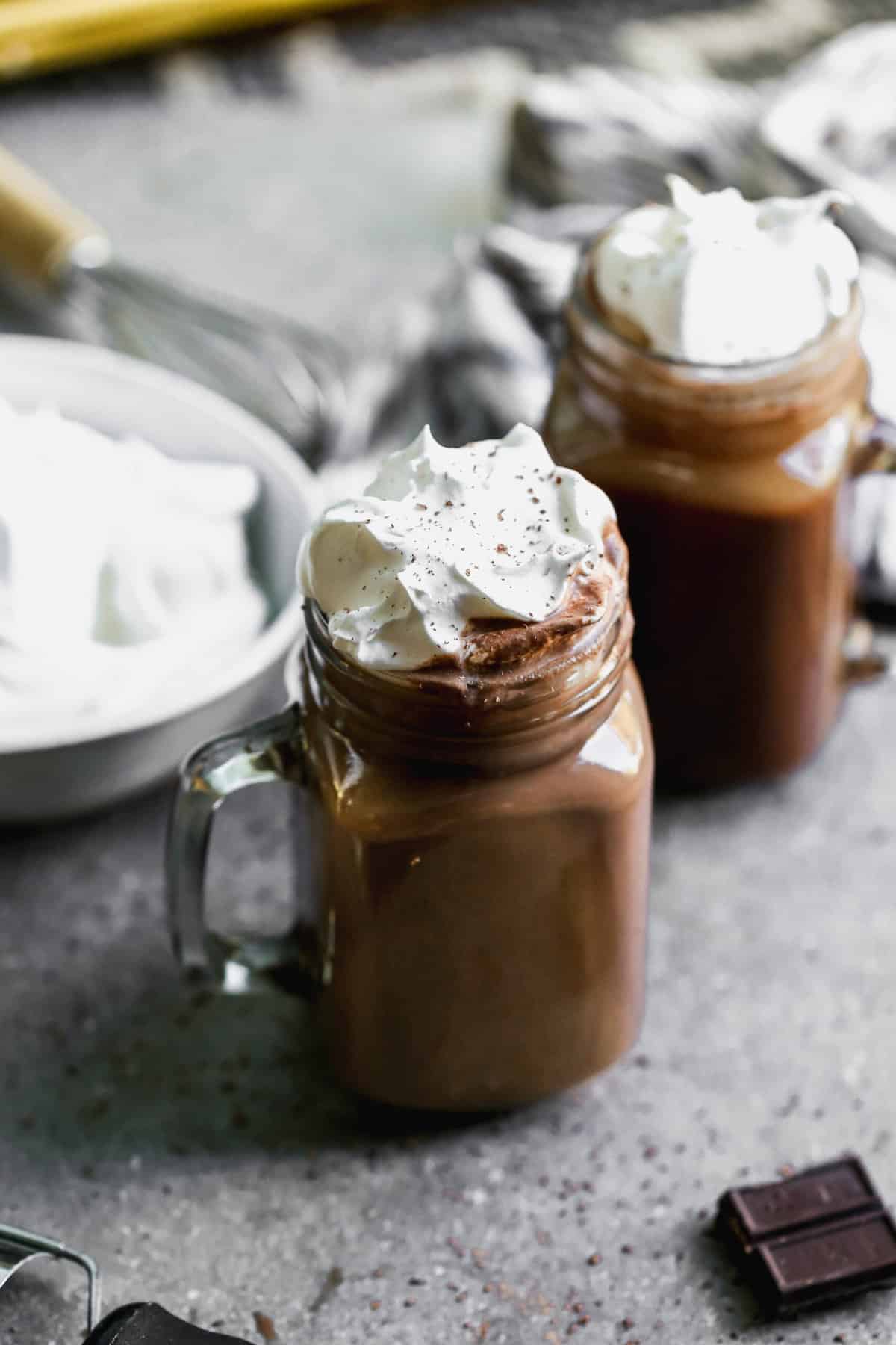 A homemade hot cocoa recipe in glass mugs, topped with fresh whipped cream.