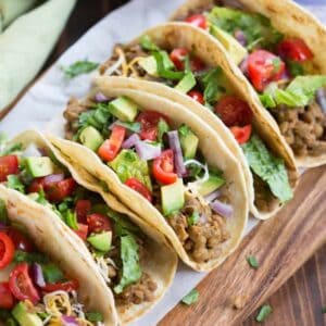 A tray full of lentil tacos made in the instant pot, served inside a tortilla, garnished with lettuce, tomato and avocado.