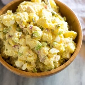 Potato salad in a wood bowl with a towel behind it.