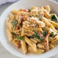 Instant Pot Tuscan Chicken Pasta on a white plate with a blue dish towel in the background.