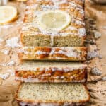 A loaf of homemade lemon poppy seed bread with a lemon glaze and a slice of lemon on top.