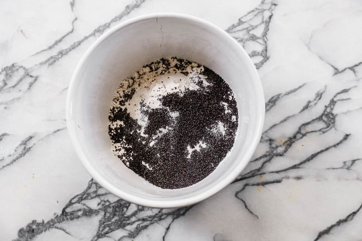 Flour, baking powder, poppy seeds, and salt in a white mixing bowl.