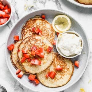 A plate with four Ricotta Pancakes on it, topped with strawberries and powdered sugar.