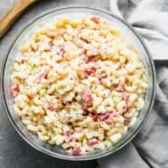 A serving bowl with macaroni salad in it and a wooden spoon on the side.