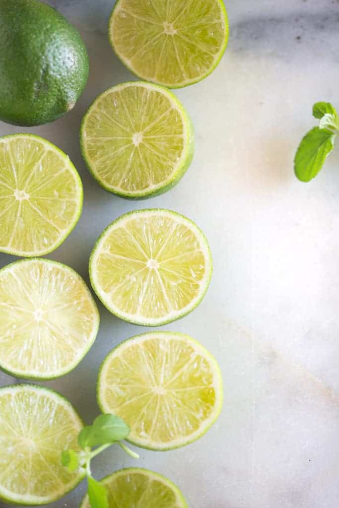 An overhead photo of sliced limes lined along a white marble board.