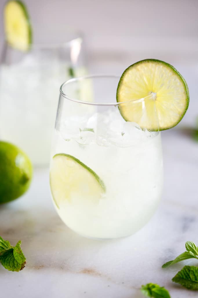 Two glasses with ice and fresh limeade, a slice of lime in the cup and a slice of lime resting on the edge.