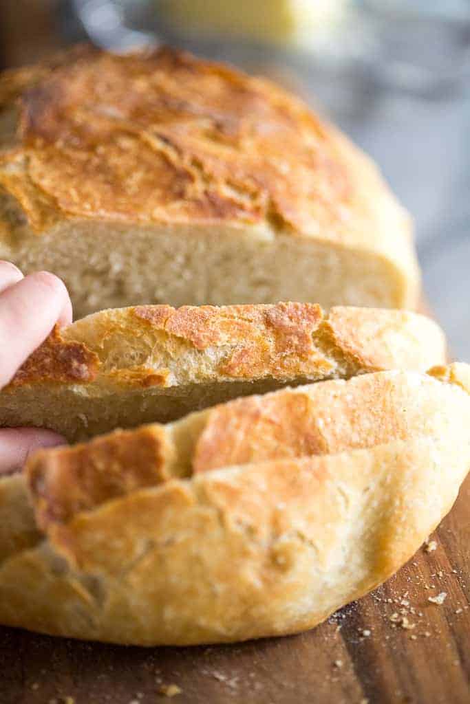 Close up photo of a loaf of no knead bread and a hand removing a slice.