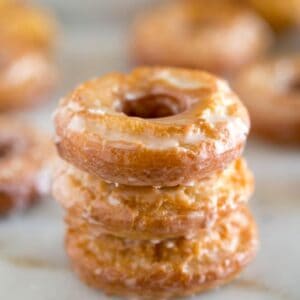 Three homemade sour cream donuts stacked on top of each other with more donuts in the background.