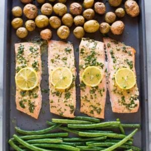 One pan baked salmon and vegetables on a large sheet pan with small red and yellow potatoes and green beans.