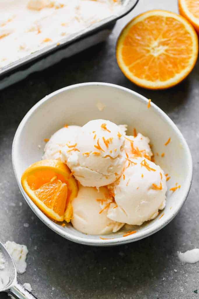 Four scoops of Orange Ice Cream served in a bowl, with an orange slice.