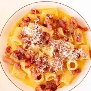 A plate of authentic Pasta Carbonara topped with crispy pancetta, pecorino cheese, and cracked black pepper.