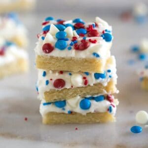 Three stacked, frosted sugar cookie bars decorated with red, white and blue sprinkles and candy on top.