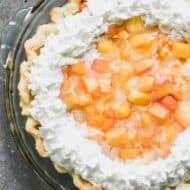 Fresh peach pie in a baked pie shell with whipped cream piped along the edges.