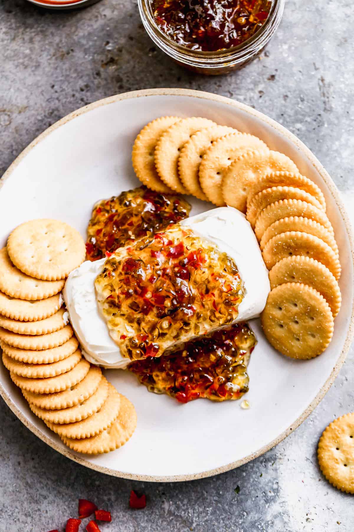 A block of cream cheese on a plate with easy pepper jelly poured on top, surrounded by ritz crackers.