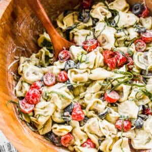 A wooden bowl filled with Pesto Tortellini salad, ready to serve.