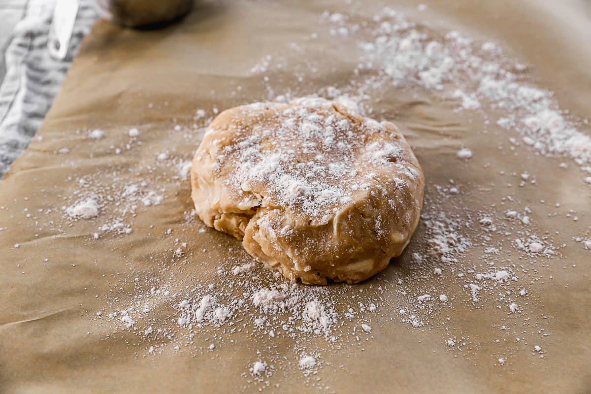 A pie crust dough disc with flour sprinkled on top, getting ready to roll out.