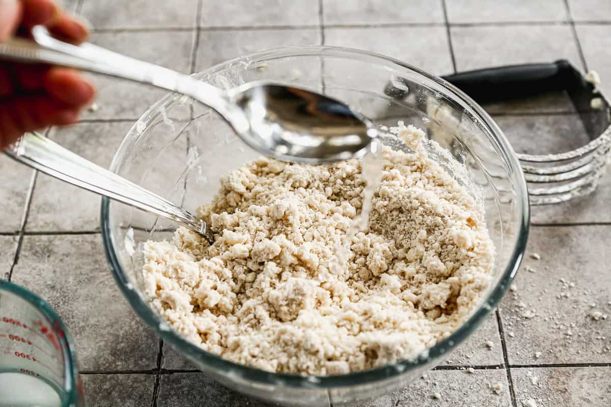 A spoon pouring ice water on a pie dough to add more moisture.