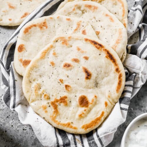 A stack of homemade Pita Breads on a dish towel, ready to eat.