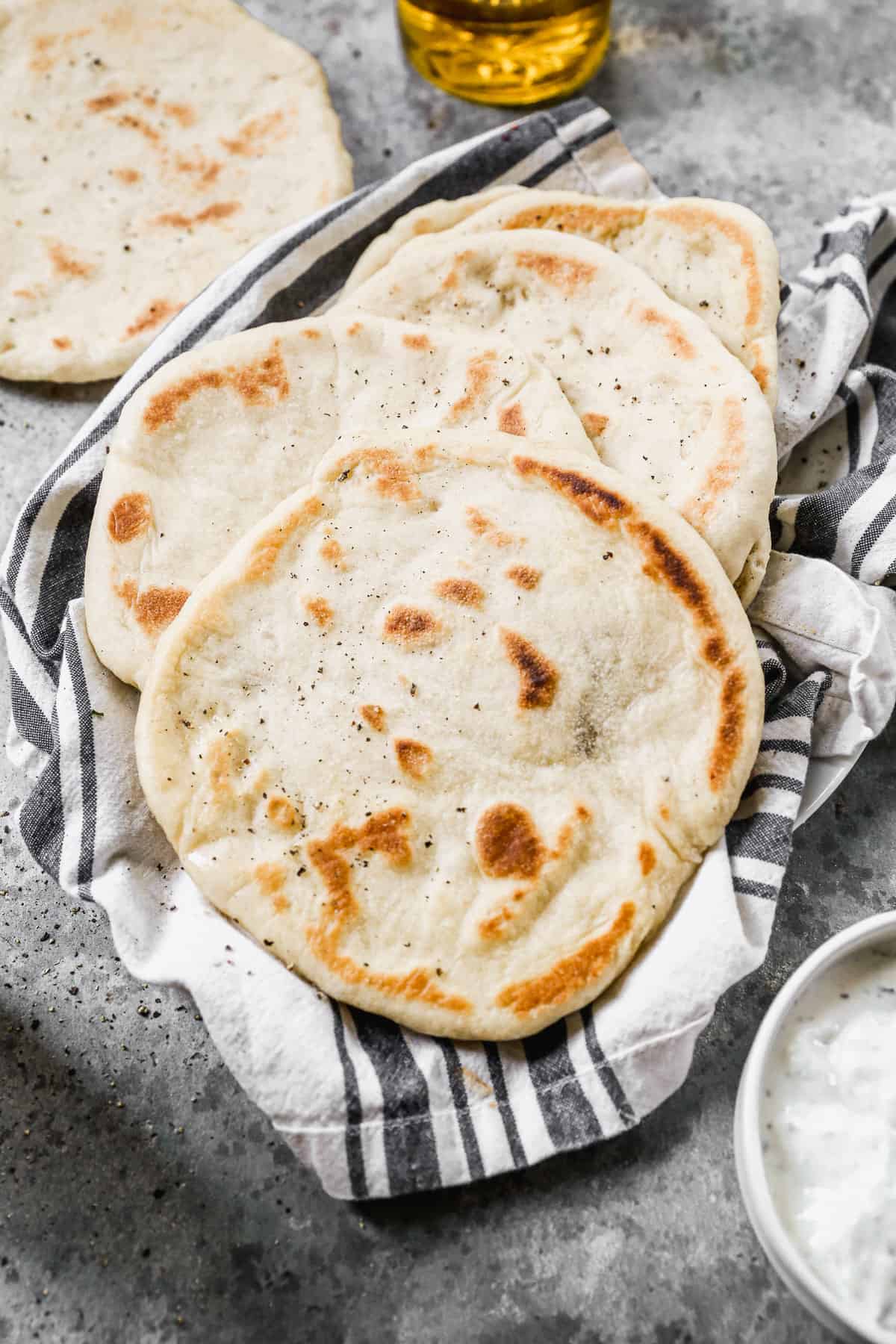 A stack of homemade Pitas on a kitchen towel, ready to eat.