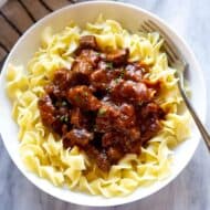 Hungarian porkolt served over egg noodles, in a bowl.