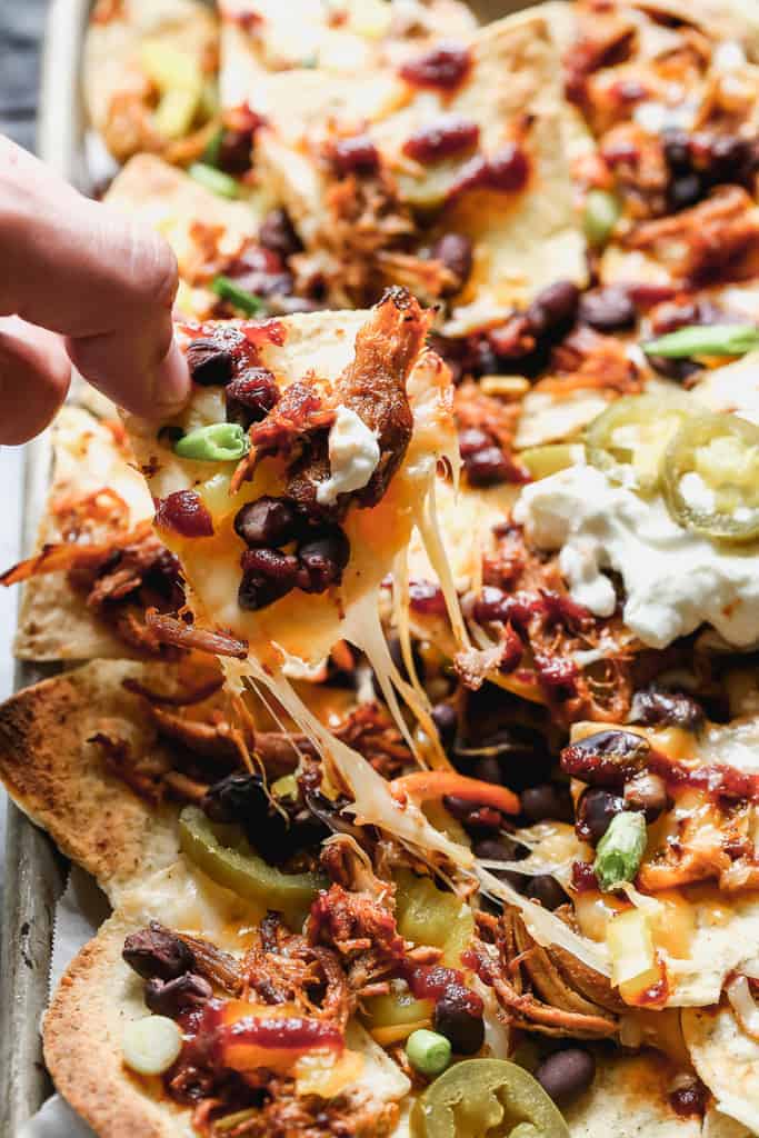 A hand pulling a nacho chip from a tray.