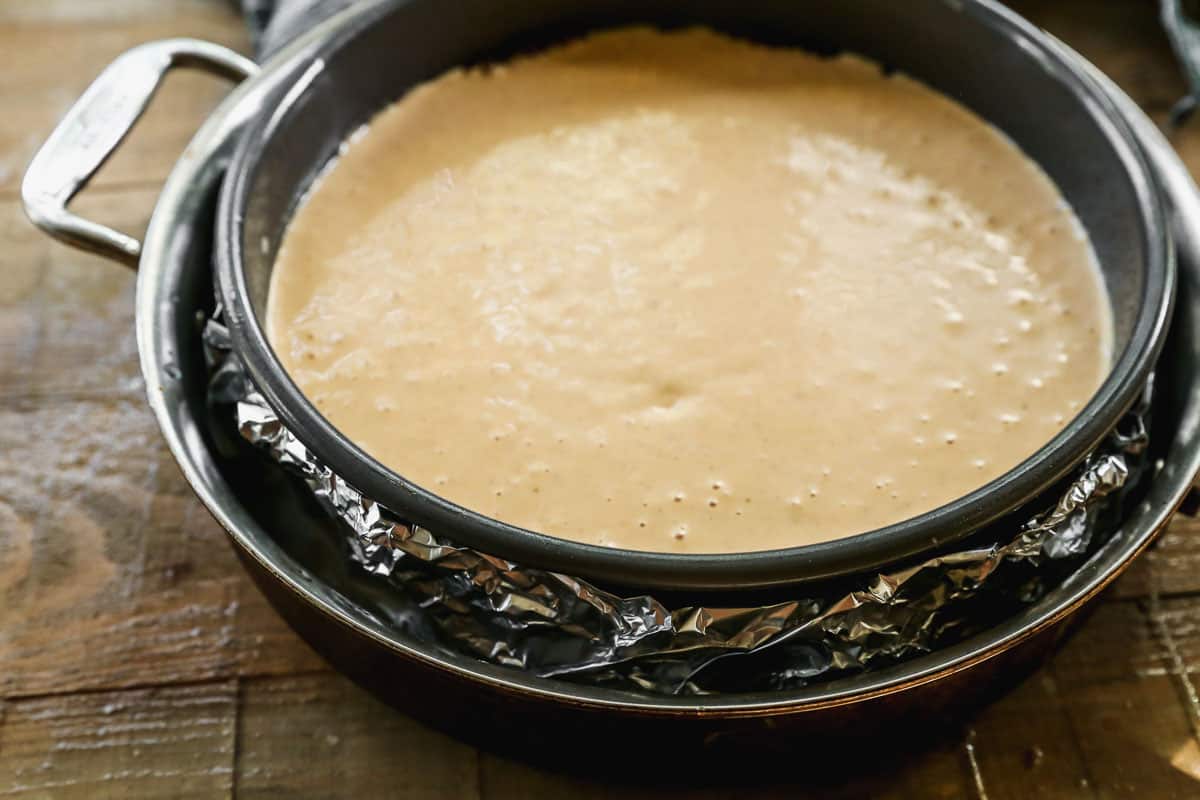 Pumpkin Cheesecake in a springform pan wrapped in tinfoil, in a larger pan for a water bath method.