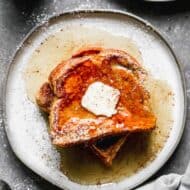 Two slices of pumpkin french toast on a plate, with syrup and butter on top.