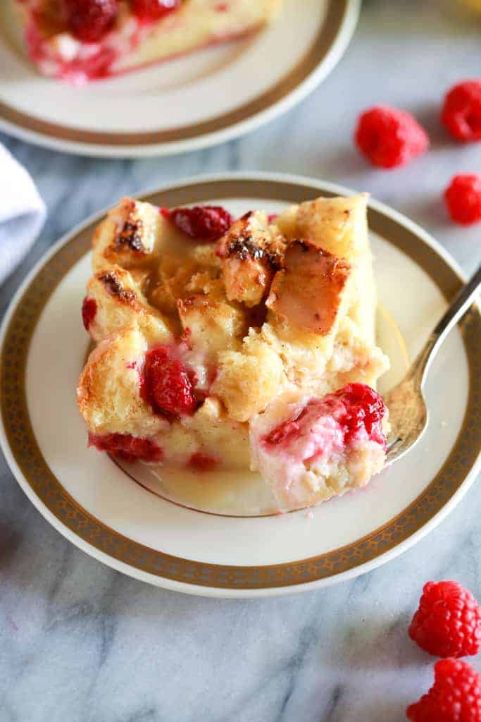 A plate with a piece of bread pudding on it and a fork taking a bite.