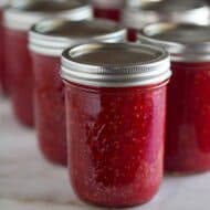 Pint jars of raspberry freezer jam lined up on a white marble board.