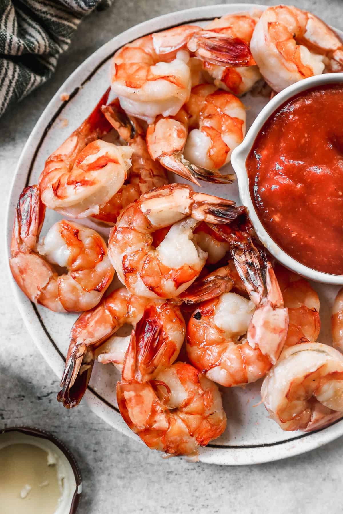 An easy Shrimp Cocktail recipe with a homemade sauce in a bowl on a platter surrounded by cooked shrimp, lemon slices, and sprigs of parsley.