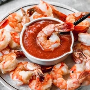 A platter of shrimp and a bowl in the middle for an easy Shrimp Cocktail sauce and one shrimp on top of the sauce.