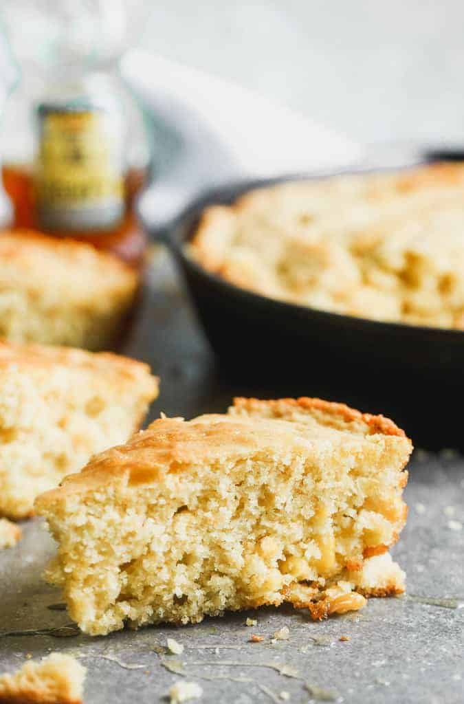 A wedge slice of skillet cornbread and cast iron skillet with cornbread in it, in the background.