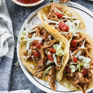 An easy slow cooker chicken tacos recipe in corn tortillas, topped with lettuce and salsa.