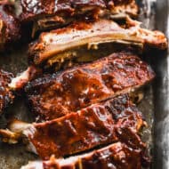 A close up image of the Best Slow Cooker Ribs on a baking sheet, smothered in homemade BBQ sauce.