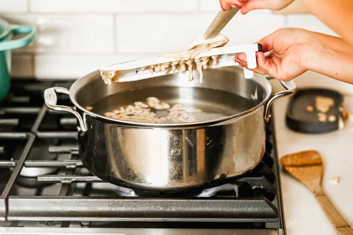 A soft dough being pushed through a cheese grater into a pot of boiling water to show how to make spaetzle.